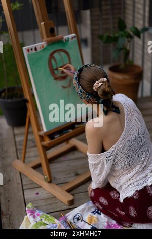 Frau Künstlerin malt auf Leinwand, Ölfarben. Staffelei auf Terrasse, Sommer. Stockfoto