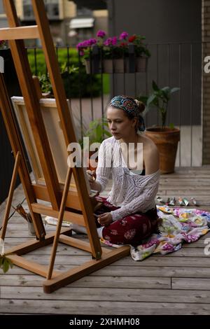 Frau Künstlerin malt auf Leinwand, Ölfarben. Staffelei auf Terrasse, Sommer. Stockfoto
