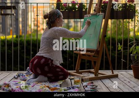 Frau Künstlerin malt auf Leinwand, Ölfarben. Staffelei auf Terrasse, Sommer. Stockfoto