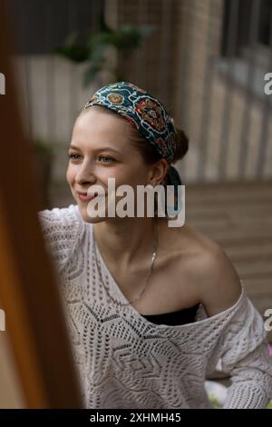 Frau Künstlerin malt auf Leinwand, Ölfarben. Staffelei auf Terrasse, Sommer. Stockfoto