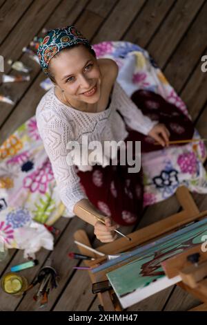 Frau Künstlerin malt auf Leinwand, Ölfarben. Staffelei auf Terrasse, Sommer. Stockfoto
