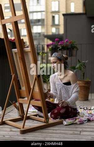 Frau Künstlerin malt auf Leinwand, Ölfarben. Staffelei auf Terrasse, Sommer. Stockfoto