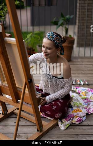 Frau Künstlerin malt auf Leinwand, Ölfarben. Staffelei auf Terrasse, Sommer. Stockfoto