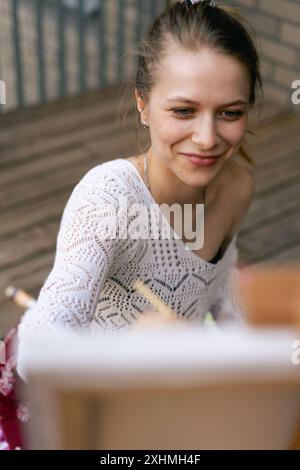 Frau Künstlerin malt auf Leinwand, Ölfarben. Staffelei auf Terrasse, Sommer. Stockfoto