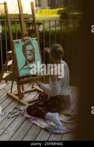 Frau Künstlerin malt auf Leinwand, Ölfarben. Staffelei auf Terrasse, Sommer. Stockfoto