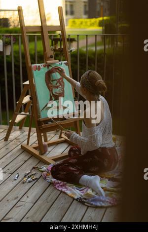 Frau Künstlerin malt auf Leinwand, Ölfarben. Staffelei auf Terrasse, Sommer. Stockfoto