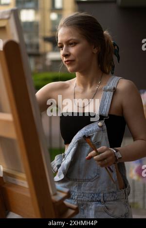 Frau Künstlerin malt auf Leinwand, Ölfarben. Staffelei auf Terrasse, Sommer. Stockfoto