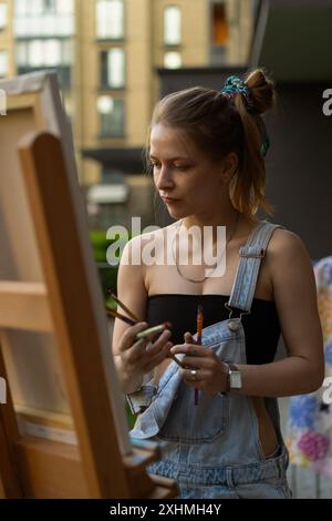 Frau Künstlerin malt auf Leinwand, Ölfarben. Staffelei auf Terrasse, Sommer. Stockfoto