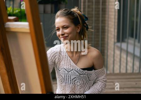 Frau Künstlerin malt auf Leinwand, Ölfarben. Staffelei auf Terrasse, Sommer. Stockfoto