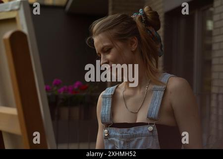 Frau Künstlerin malt auf Leinwand, Ölfarben. Staffelei auf Terrasse, Sommer. Stockfoto