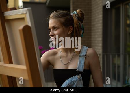 Frau Künstlerin malt auf Leinwand, Ölfarben. Staffelei auf Terrasse, Sommer. Stockfoto