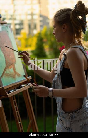 Frau Künstlerin malt auf Leinwand, Ölfarben. Staffelei auf Terrasse, Sommer. Stockfoto