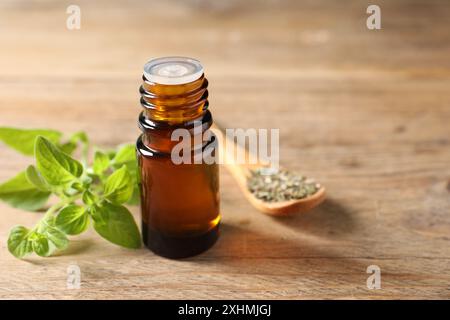 Ätherisches Öl in der Flasche, Löffel mit trockenem Kraut und Oregano-Zweigen auf Holztisch, Nahaufnahme. Leerzeichen für Text Stockfoto