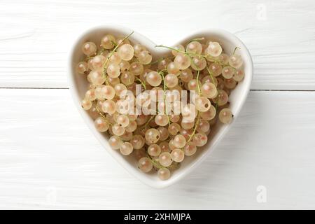 Frische weiße Johannisbeeren in einer herzförmigen Schüssel auf weißem Holztisch, Blick von oben Stockfoto