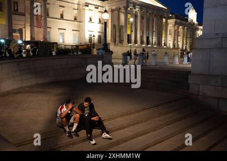 Zwei niedergeschlagene englische Fußballfans sitzen während eines Polizeieinsatzes auf den Treppen auf dem Trafalgar Square im Falle einer Massenstörung in den Stunden nach der Niederlage Englands gegen Spanien im UEFA-Cup-Finale am 14. Juli 2024 in London. Es wurden keine Probleme gemeldet und Fußballfans gingen größtenteils leise nach Hause. Stockfoto