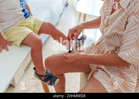 Mutter, Kind und Schuhe in Vorbereitung auf Schule, Lernen oder Bildung im Wohnzimmer zu Hause. Mom hilft dem kleinen Jungen mit Schuhen, sich darauf vorzubereiten Stockfoto