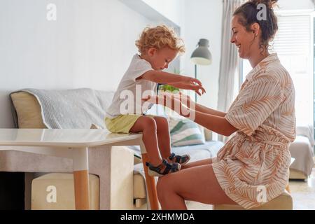 Mutter, Kind und Schuhe in Vorbereitung auf Schule, Lernen oder Bildung im Wohnzimmer zu Hause. Mom hilft dem kleinen Jungen mit Schuhen, sich darauf vorzubereiten Stockfoto