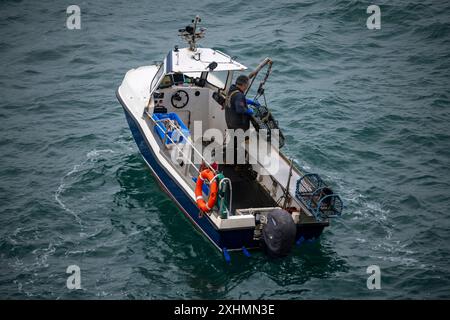 Kleines Fischerboot vor der Küste von Anglesey, Nordwales. Ein einziger Fischer inspiziert Hummertöpfe. Stockfoto