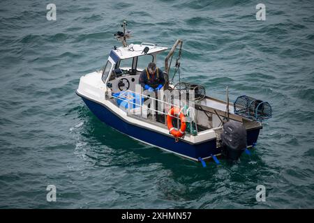 Kleines Fischerboot vor der Küste von Anglesey, Nordwales. Ein einziger Fischer inspiziert Hummertöpfe. Stockfoto