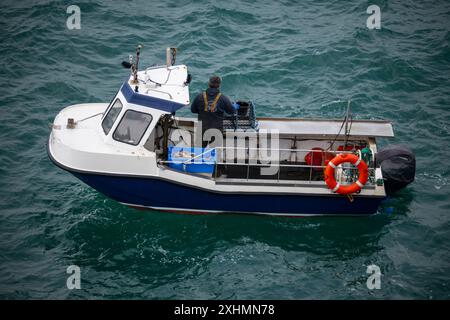 Kleines Fischerboot vor der Küste von Anglesey, Nordwales. Ein einziger Fischer inspiziert Hummertöpfe. Stockfoto