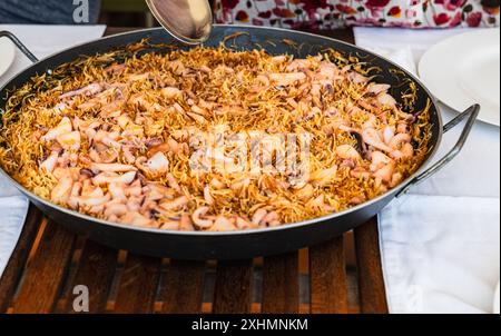 Eine große Pfanne mit traditionellen Meeresfrüchtenudeln wird auf einem hölzernen Esstisch serviert. Stockfoto
