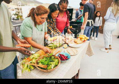 Generationenübergreifende Menschen, die auf dem Dach des Hauses grillen - multirassische Freunde, die am Wochenende Spaß beim Essen und Kochen haben - Sommer und Stockfoto