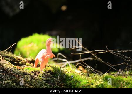 Spielzeug-Dinosaurier auf moosigem Baumstamm in Waldszene im Sonnenlicht. Stockfoto