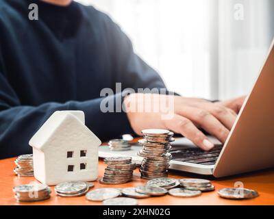 Immobilieninvestitionen, Ersparnisse, Einkommen, Immobilienpreiswert, Immobiliengewinnkonzepte. Weißes Miniaturmodell und Münzstapel auf Holzschreibtisch Stockfoto