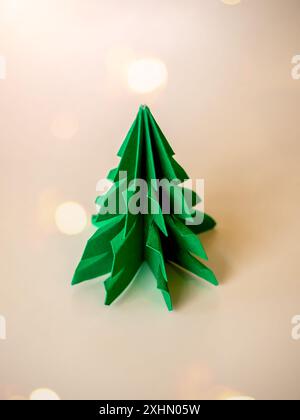 Frohe Weihnachten und Happy New Year Konzept, minimalistischer Stil. Grüner Origami-Papier-Weihnachtsbaum isoliert auf weißem Hintergrund mit festlichem Licht Bokeh am Stockfoto