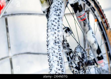 Nahaufnahme des Radrads in der Autowaschanlage. Waschen Sie das Fahrrad mit einem Strahl aus weißem Schaum. Wartung Stockfoto