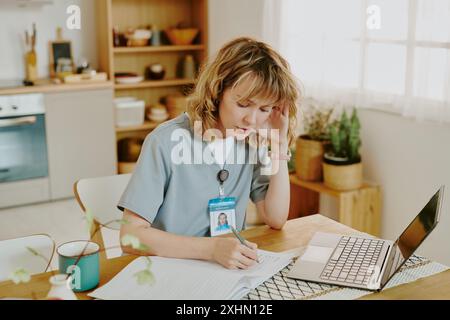 Fokussierte kaukasische Krankenschwester, die nach der Arbeit zu Hause medizinische Karten ausfüllt Stockfoto