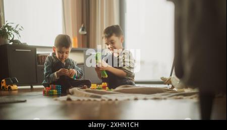 Porträt zweier männlicher asiatischer Kinder, die während des Sonnentages mit bunten Bausteinen in ihrem Zimmer spielen. Bruder hilft jüngeren Geschwistern, ein Spielzeughaus zu bauen. Kindheit und Unschuld Stockfoto