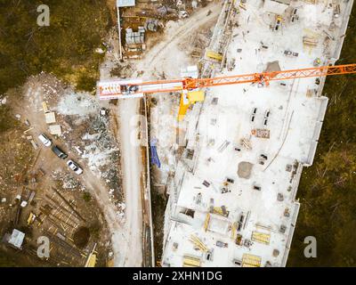 Baustelle mit statischer Sicht aus der Luft ein einziger Bauarbeiter auf dem Dach errichtet ein hohes Gewerbeimmobiliengebäude in grünen Vororten der Stadt. C Stockfoto