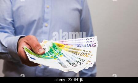 Ein nicht erkennbarer Mann hält einen Haufen Euro in der Hand und gibt sie jedem. Stockfoto