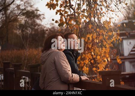 Glückliches verheiratetes Paar über 50 Jahre alt, das im Herbst an einem warmen, sonnigen Abend am Ufer des Parks entlang spaziert, zuhört und den Herbst beobachtet. hap Stockfoto