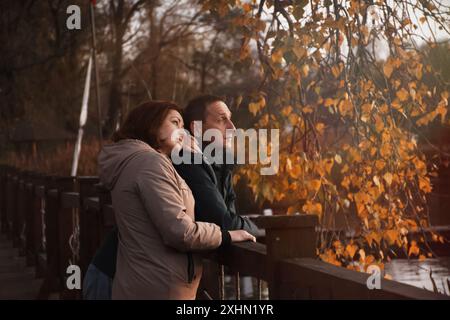 Glückliches verheiratetes Paar über 50 Jahre alt, das an einem warmen, sonnigen Abend im Herbst entlang des Damms im Park spaziert und umarmt. Im Herbst. Glückliche Familie Stockfoto