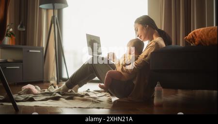 Arbeiten von zu Hause aus: Porträt der jungen asiatischen Mutter, die ihr süßes Baby hält und tagsüber an einem Laptop arbeitet. Erfolgreiche Architektin für Frauen, die Leben und Arbeit in Einklang bringen, während sie ihre Arbeit aus der Ferne erledigen. Stockfoto