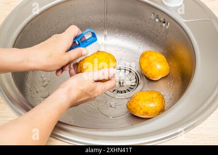 Die Hausfrau wäscht frische Kartoffeln in der Küchenspüle. Stockfoto