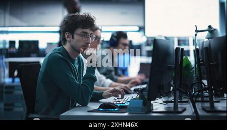 Porträt eines nachdenklichen jungen Ingenieurs, der am Computer in einer technologischen Büroumgebung arbeitet. Junge Frau, die Kopfhörer trägt, schreibt Software-Code für ein innovatives Internet-Projekt Stockfoto