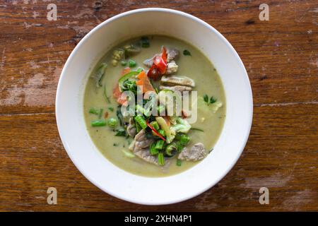 Grüne Currysuppe mit Hühnchen auf weißem Teller und braunem Holztisch. Draufsicht. Thailändische Küche. Stockfoto