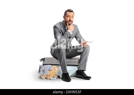 Besorgter Geschäftsmann sitzt auf einem Koffer und wartet auf einen Flug isoliert auf weißem Hintergrund Stockfoto