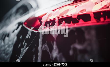 Bremslicht in einem modernen schwarzen Auto. Nahaufnahme ästhetisches Foto eines Fahrzeugs in einer Autowaschanlage. Makroaufnahme von Autoteilen, die mit Seifenwasser bedeckt sind. Werbung für ein Detailstudio oder einen Autohersteller Stockfoto