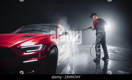 Porträt eines erwachsenen Mannes, der in einem Detailstudio arbeitet und einen Factory Fresh Red Sportscar für Wartungsarbeiten und Autopflege vorbereitet. Reinigungstechniker Mit Hochdruckreiniger Stockfoto