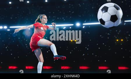 Ästhetischer Schuss des weiblichen Fußballspielers, der auf schwarzem Hintergrund unter Spotlight springt und tritt. Professionelle Sportfrau, die Ein wunderschönes Tor im internationalen Meisterschaftsspiel erzielt. Stockfoto