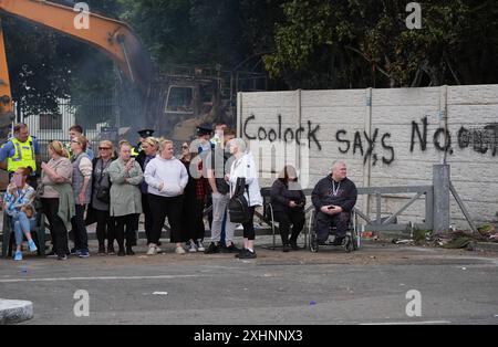 Die Menschen sehen zu, wie Demonstranten mit Gardai abtreten, nachdem am ehemaligen Standort der Crown Paintfabrik in Coolock, Nord-Dublin, eine Reihe von Bränden ausgebrochen sind. Bilddatum: Montag, 15. Juli 2024. Stockfoto