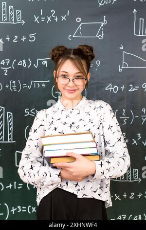 Ein Schulmädchen steht neben der Tafel mit einem Lehrbuch in der Hand, Porträt eines Teenagers in der Schule. Stockfoto