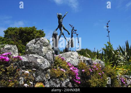 Die Statuen von Kindern, die von dem Bildhauer David Wynne spielen, überblickten die blumenbedeckte Granitwand der Abteigärten auf der Insel Tresco in Th Stockfoto