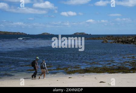 Ein paar Spaziergänger genießen die Ruhe und Ruhe, die auf dem weißen Sand und den Muscheln am Strand von Pelistry Bay mit den Eastern Isles in der dista spazieren Stockfoto