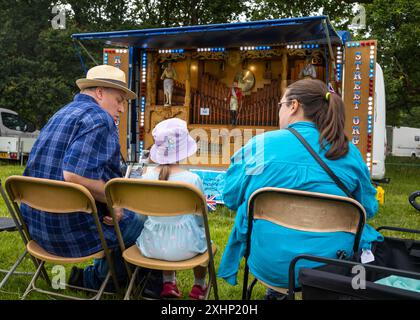 Storrington / Vereinigtes Königreich - 13. Juli 2024: Ein junges Mädchen und ihre Großeltern hören auf der Sussex Steam Fair, Parham, Storrington, eine traditionelle Orgel auf dem Festplatz. Stockfoto