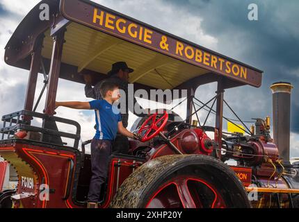 Parham/UK - 13. Juli 2024: OMON, ein dampfbetriebener Marshall Road Roller aus dem Jahr 1926, wird von einem jungen Jungen auf der Sussex Steam Fair in Storrington, Großbritannien gefahren. Stockfoto